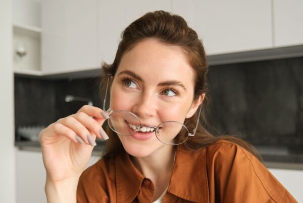 close up portrait of a woman holding glasses and smiling for a blog post titled Finding an Invisalign Dentist Near Me