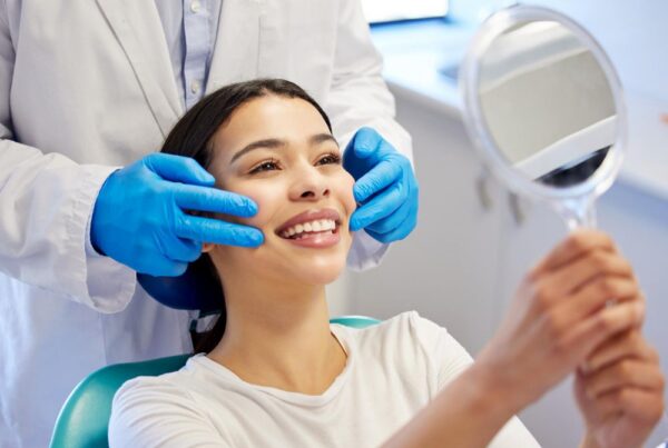 A woman in a dental chair smiling in a hand mirror for a blog post titled, "How Do I Find the Best Cosmetic Dentist Near Me?"